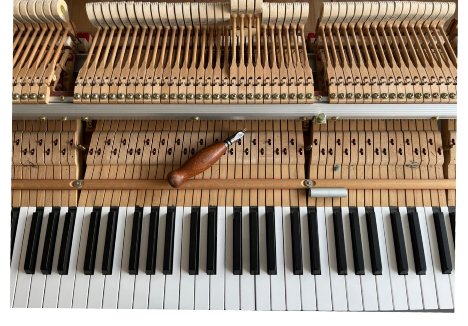 Clavier et mécanique d'un piano droit ouverts, vus du dessus, un outil de réglage posé